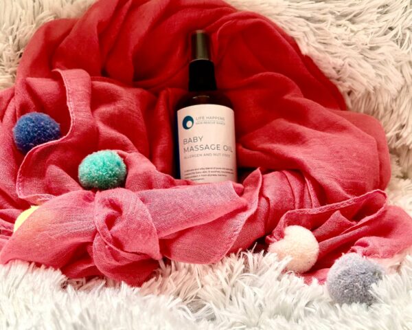 A bottle of baby massage oil and a lovely pink scarf, ideal for nurturing moments and relaxation.